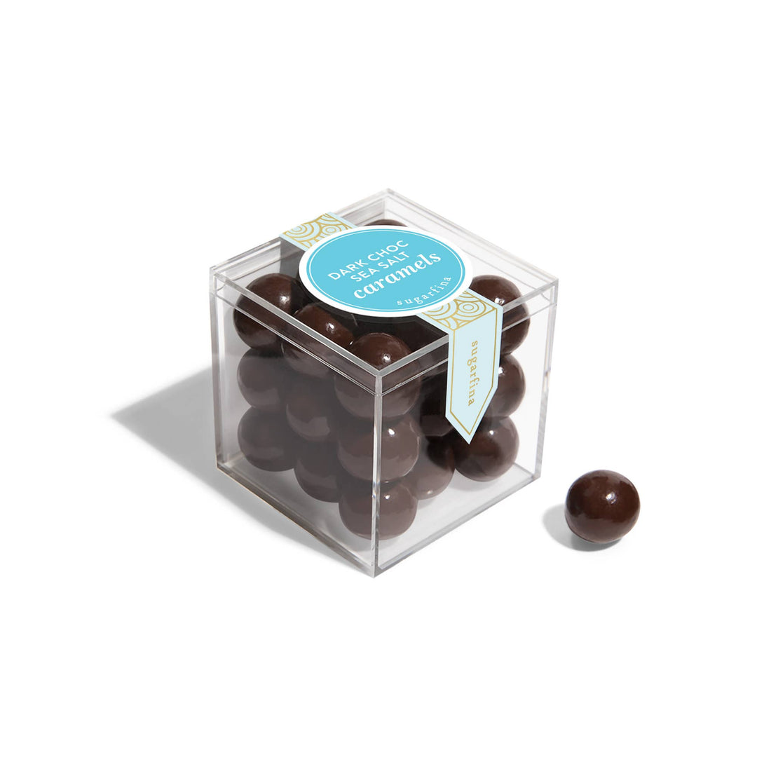 Clear cube box filled with chocolate-covered caramels on a white background