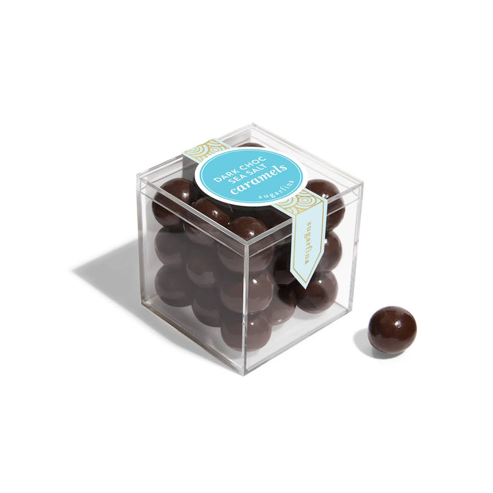 Clear cube box filled with chocolate-covered caramels on a white background