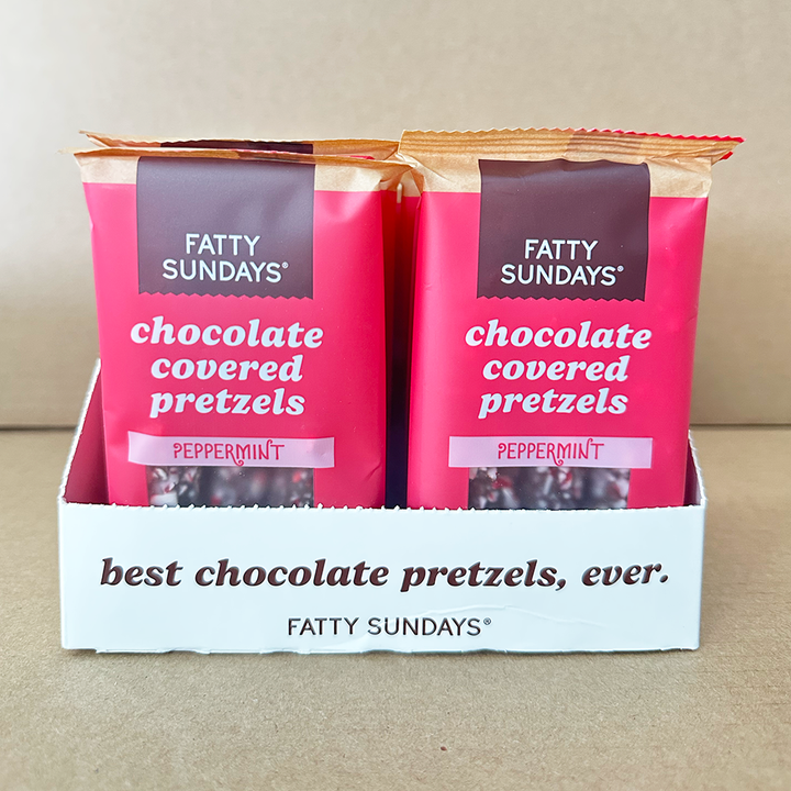 Two packages of Fatty Sundays chocolate covered pretzels in a display box on a beige background.