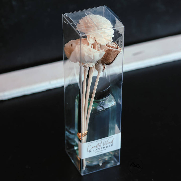 Decorative diffuser with dried flowers in a clear packaging on a dark surface.