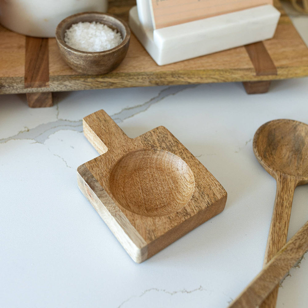 Wooden dish and spoon on a marble surface with wooden accents in the background.