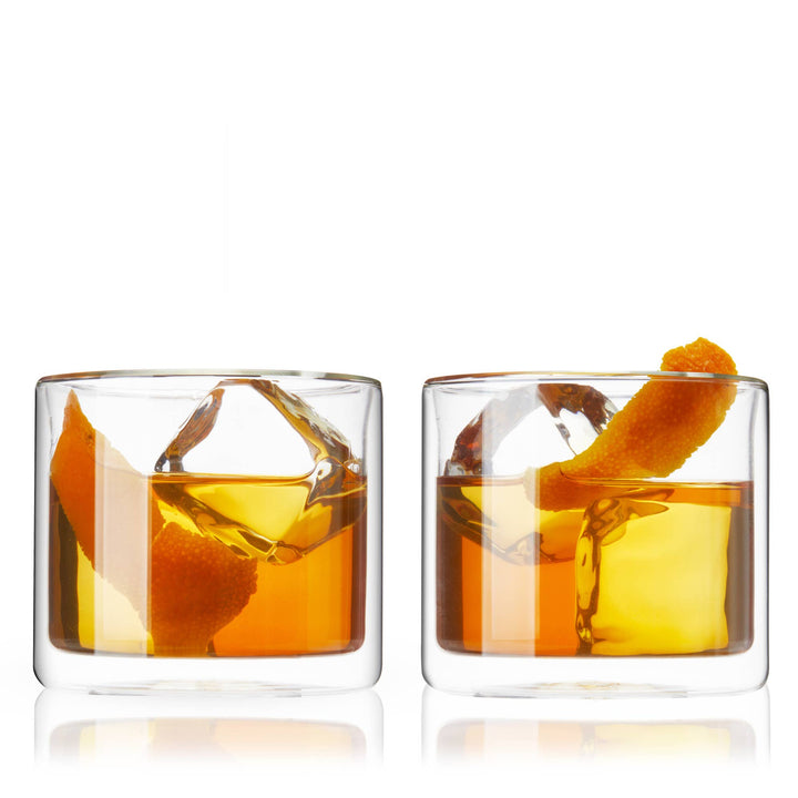 Two glasses of orange liqueur with orange peels on a white background