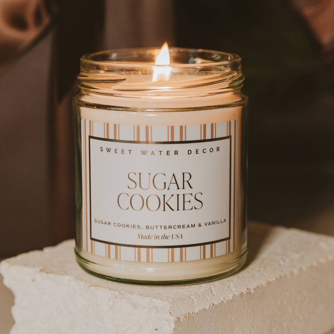 Candle in a jar labeled 'Sugar Cookies' by Sweet Water Decor on a neutral background