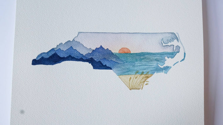 Map of North Carolina with a sunset over mountains and ocean on a white background