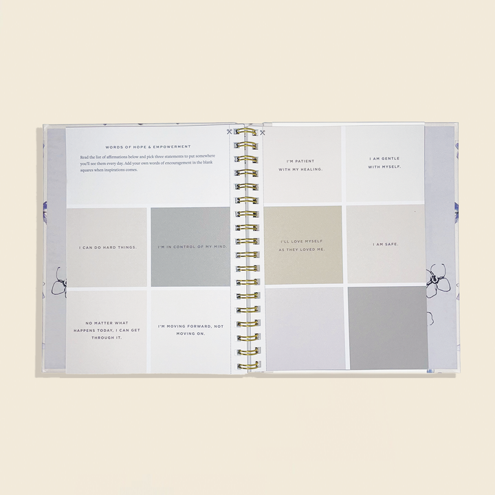 Open spiral-bound book with motivational phrases on a beige background