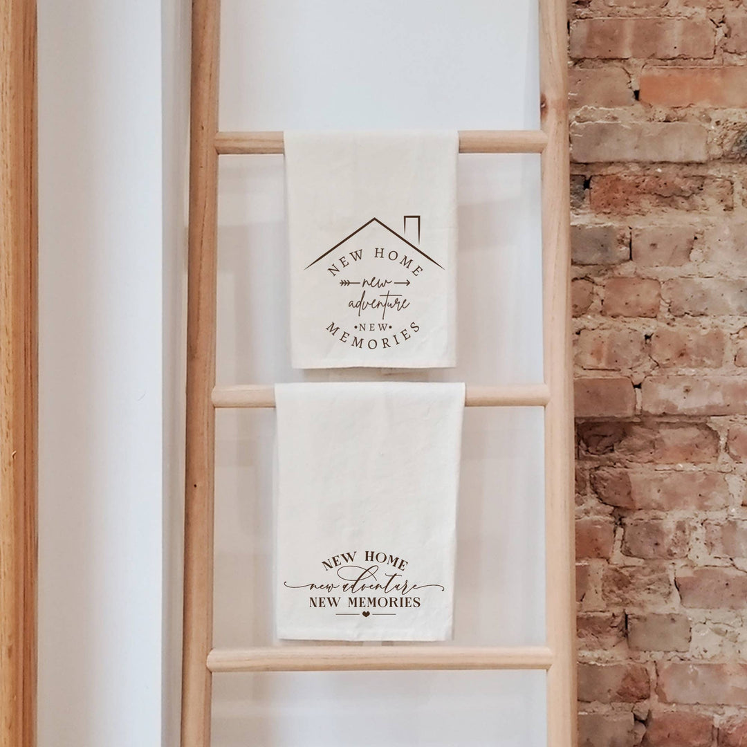 Two towels with housewarming messages on a wooden ladder against a brick wall.