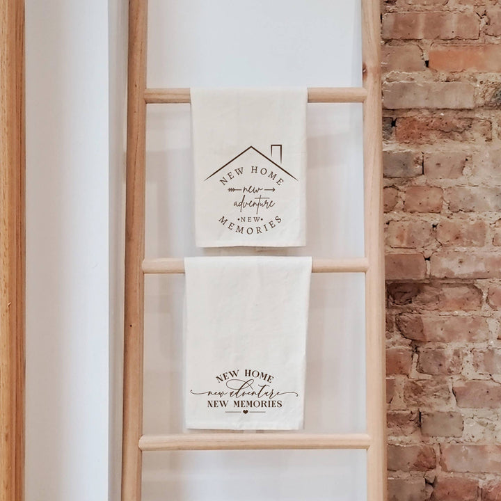 Two towels with housewarming messages on a wooden ladder against a brick wall.