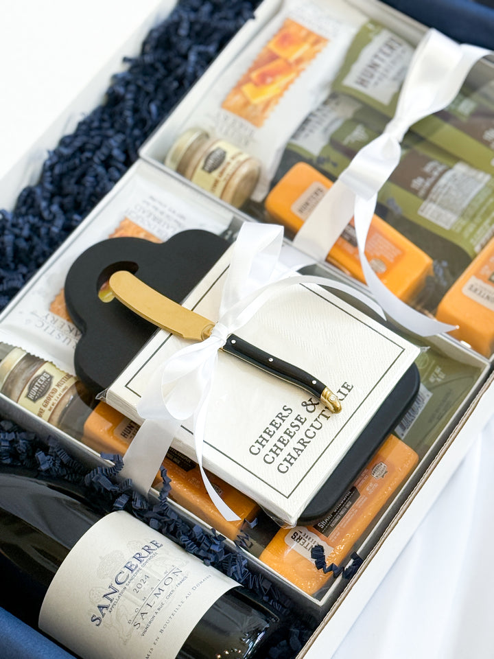 Gift set with Sancerre wine, cheese board with napkins, and a charcuterie kit on a blue textured surface. 