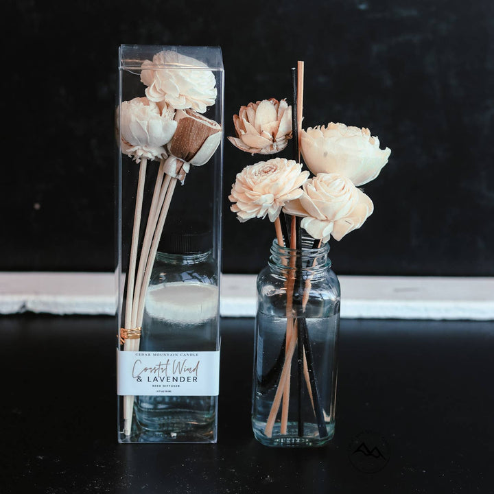 Decorative diffuser with flowers in a clear bottle on a dark surface