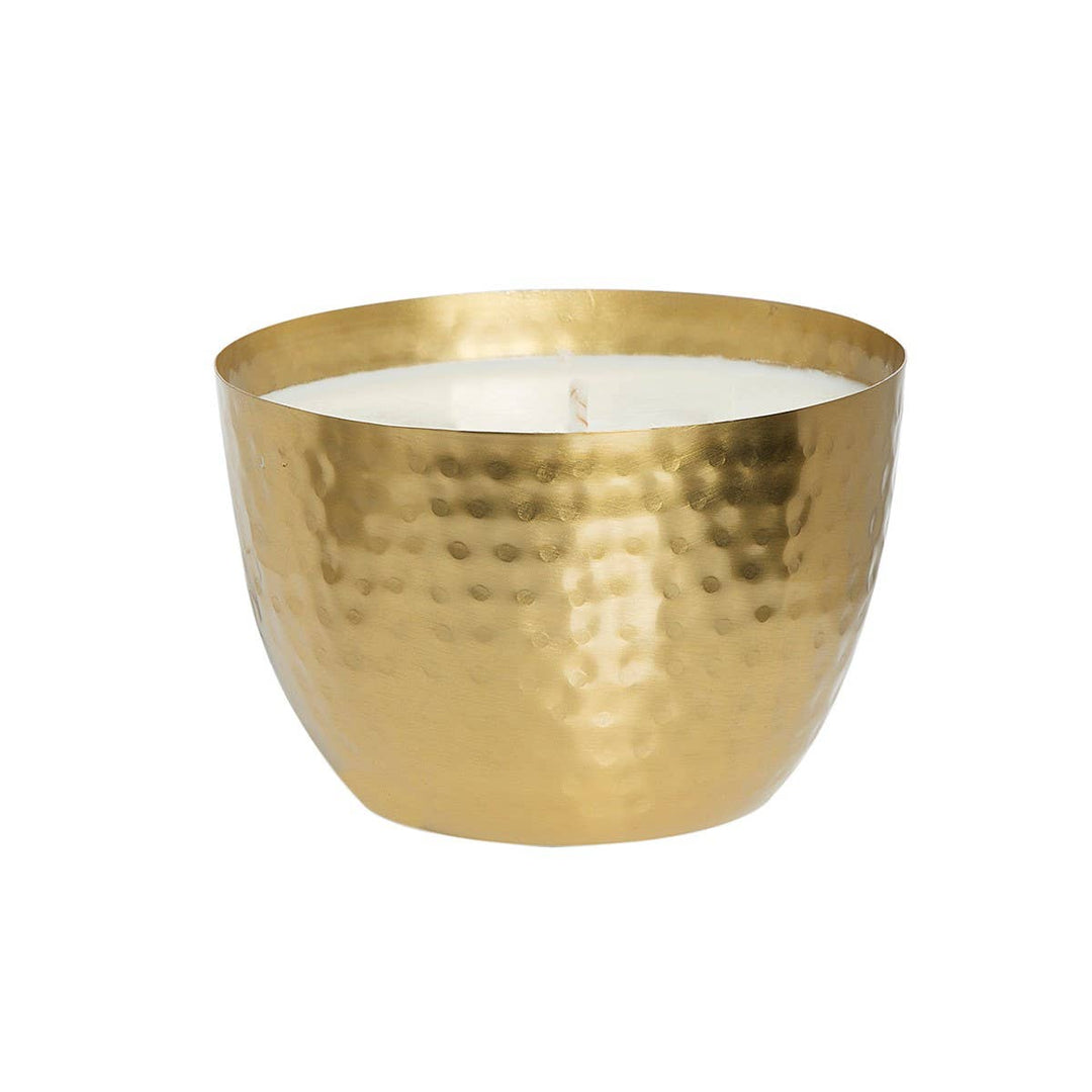 A gold hammered metal bowl containing a white soy candle.