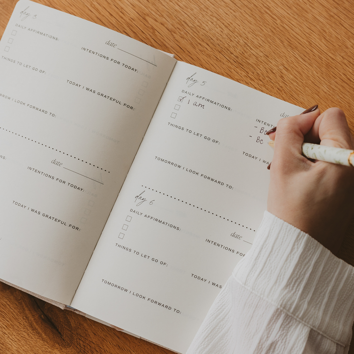 Person writing in a daily journal on a wooden surface