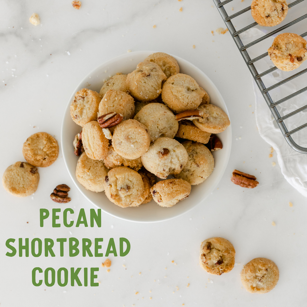 Pecan shortbread cookies in a white bowl with a cooling rack and scattered cookies on a light surface.