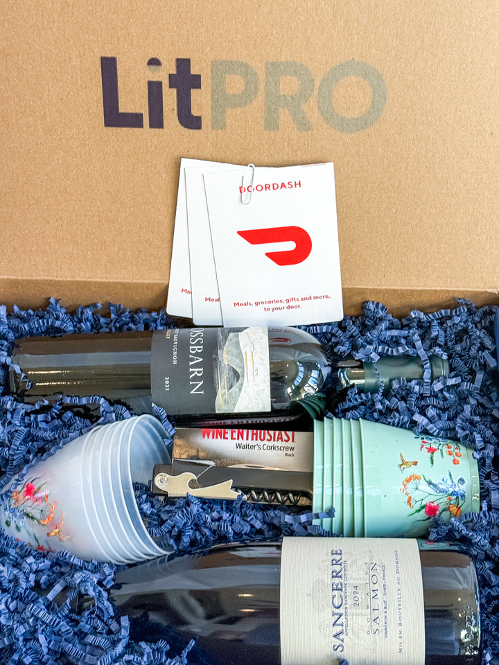 LitPro gift box with wine bottles, cups, a corkscrew and gift cards on blue crinkle paper. 