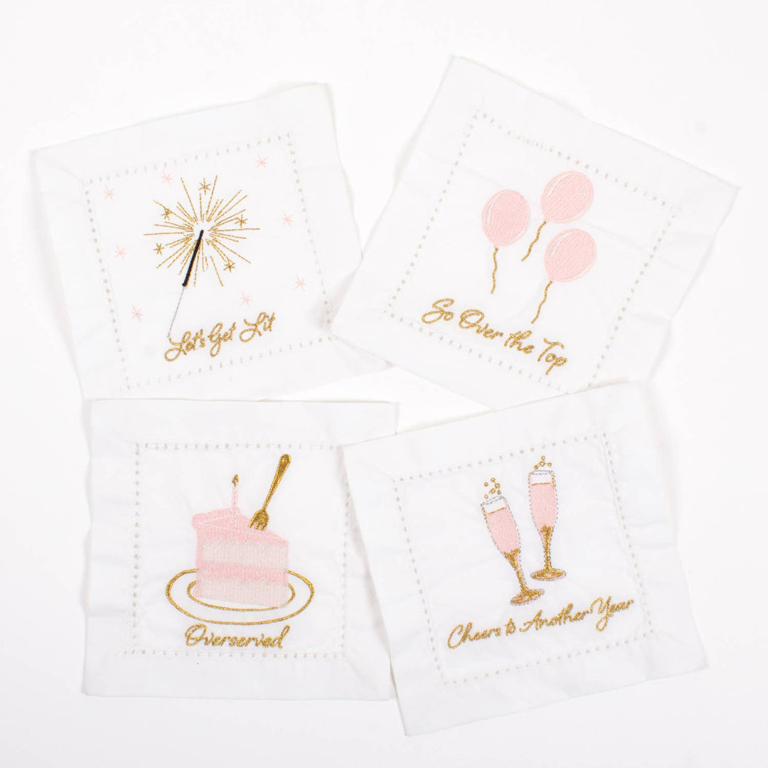 Set of four white napkins with pink and gold celebratory designs and text on a white background