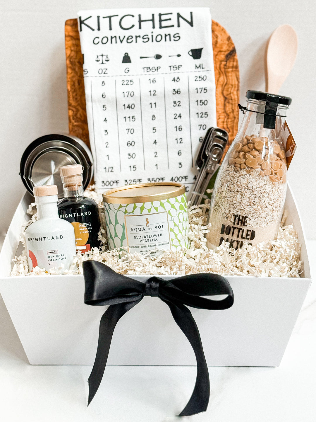 Savor & Style Kitchen Gift Basket shrink-wrapped with bow, includes rustic olive wood cutting board, gourmet cookie mix, candle, and kitchen essentials