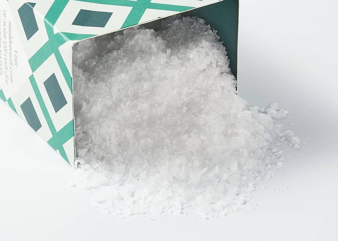White sea salt spilling out of a green and white container on a white background