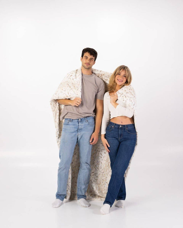 Two people standing together with a blanket draped over them on a white background