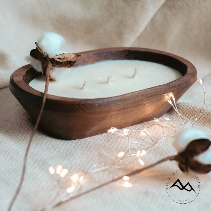 Wooden dough bowl candle on a textured surface with fairy lights