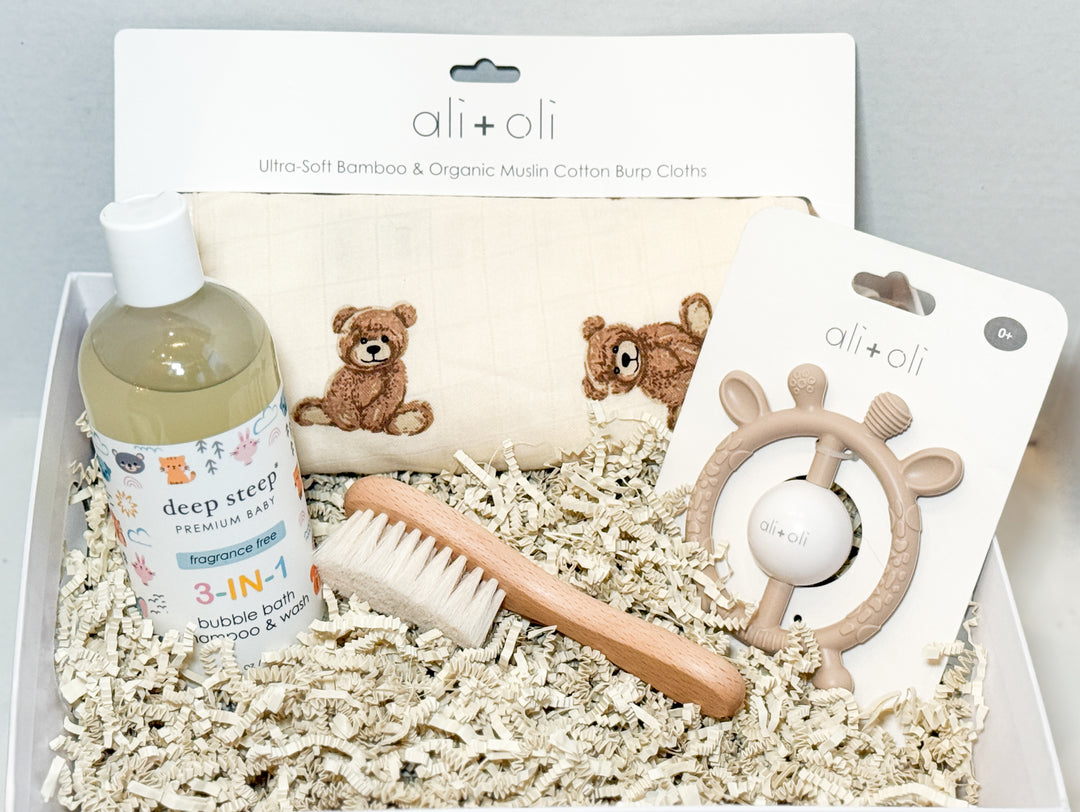 Basket of baby care products including a 3-in-1 wash, brush, teddy bear burp cloths and a teether with &