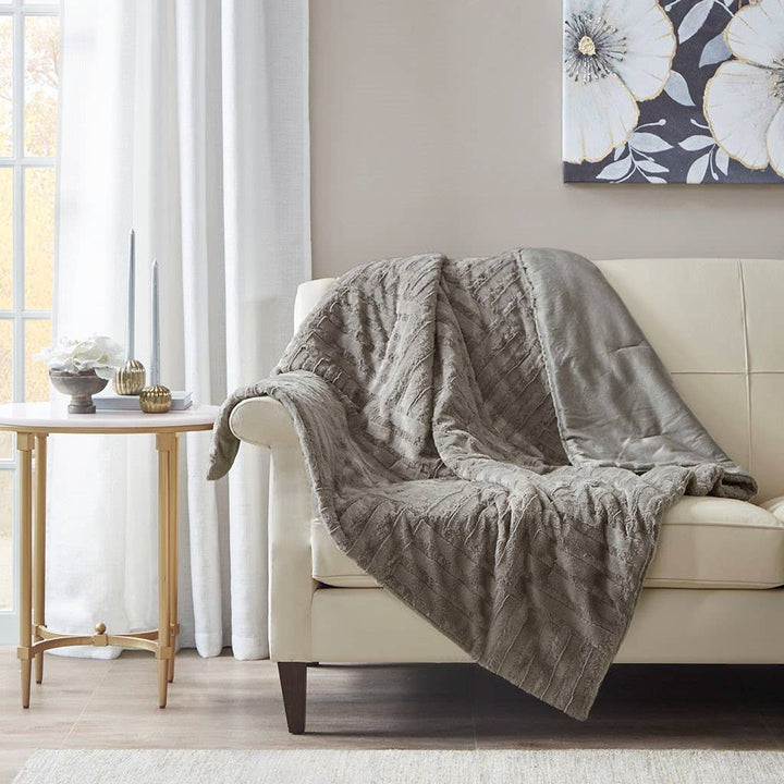 Gray textured blanket draped over a beige sofa in a living room setting.