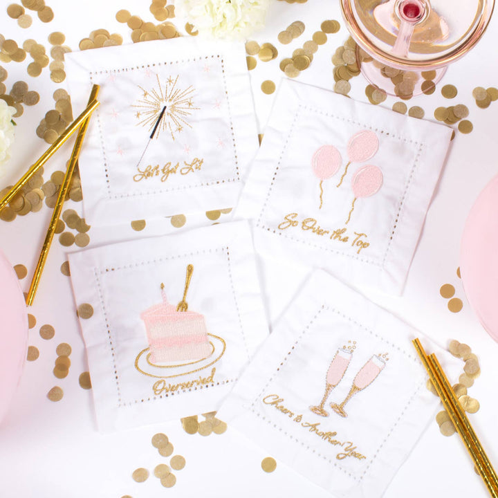 Decorative cocktail napkins with celebratory designs on a table with confetti and drinks.