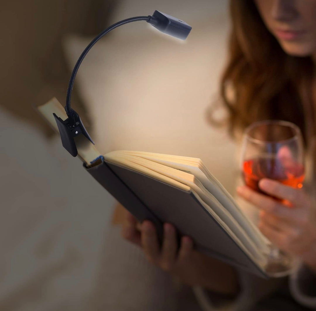 Person reading a book with a clip-on reading light and holding a glass of wine.