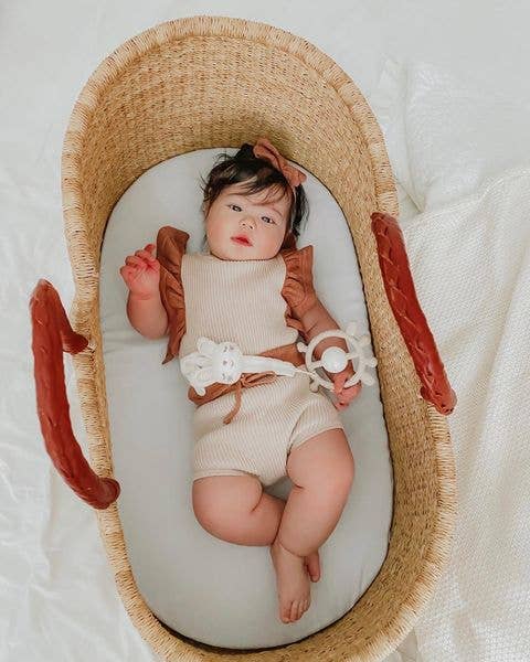 Baby lying in a woven basket wearing a beige outfit with ruffled sleeves.
