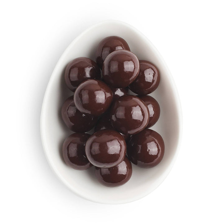 Chocolate-covered caramels in a white bowl on a white background
