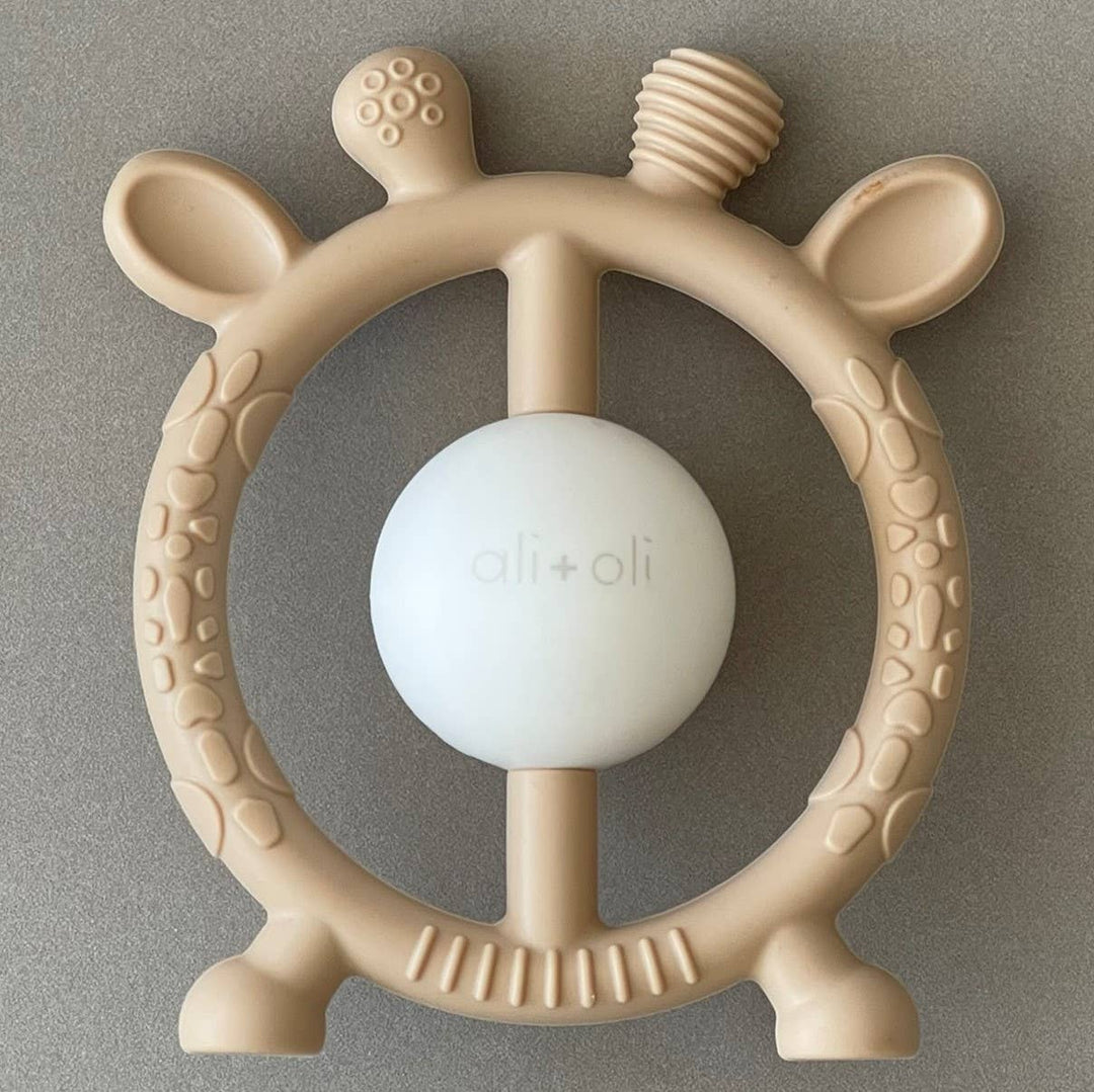 Beige steering wheel-shaped teething ring with a white center on a gray background