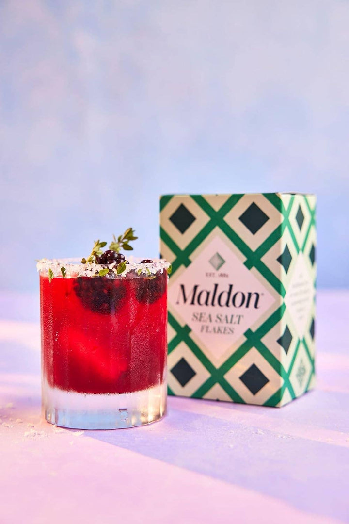Red cocktail in a glass with Maldon sea salt flakes container on a light background