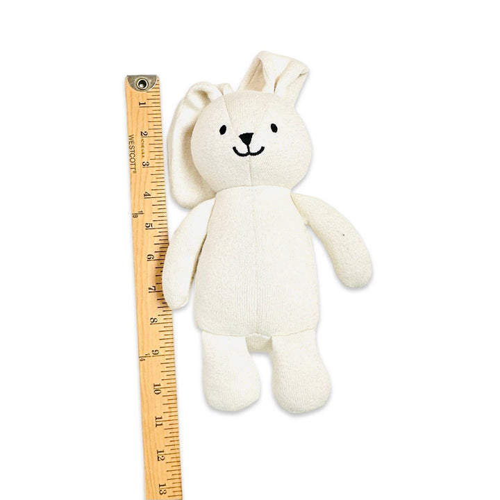 White plush toy next to a wooden ruler on a white background