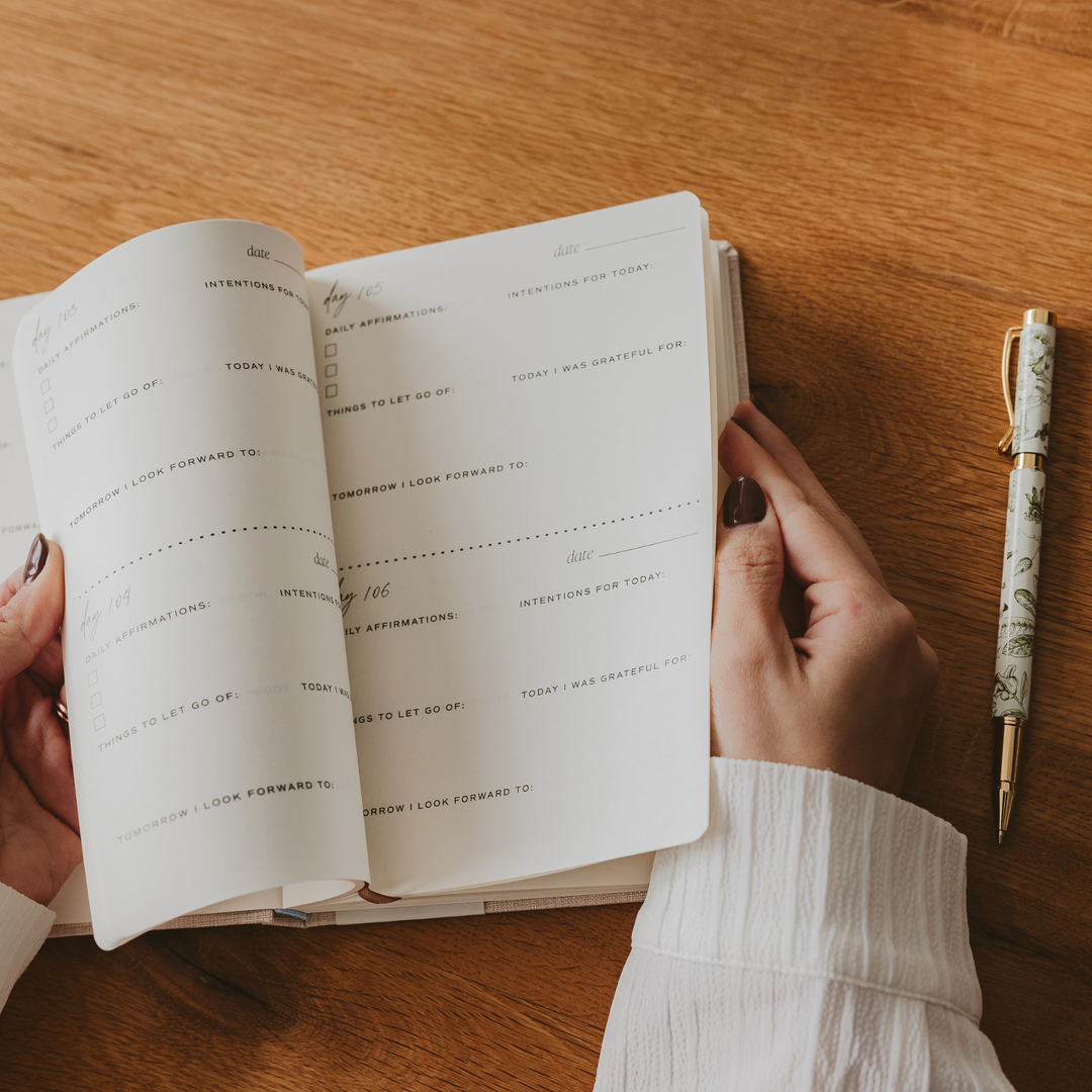 Person holding an open journal with a pen on a wooden surface
