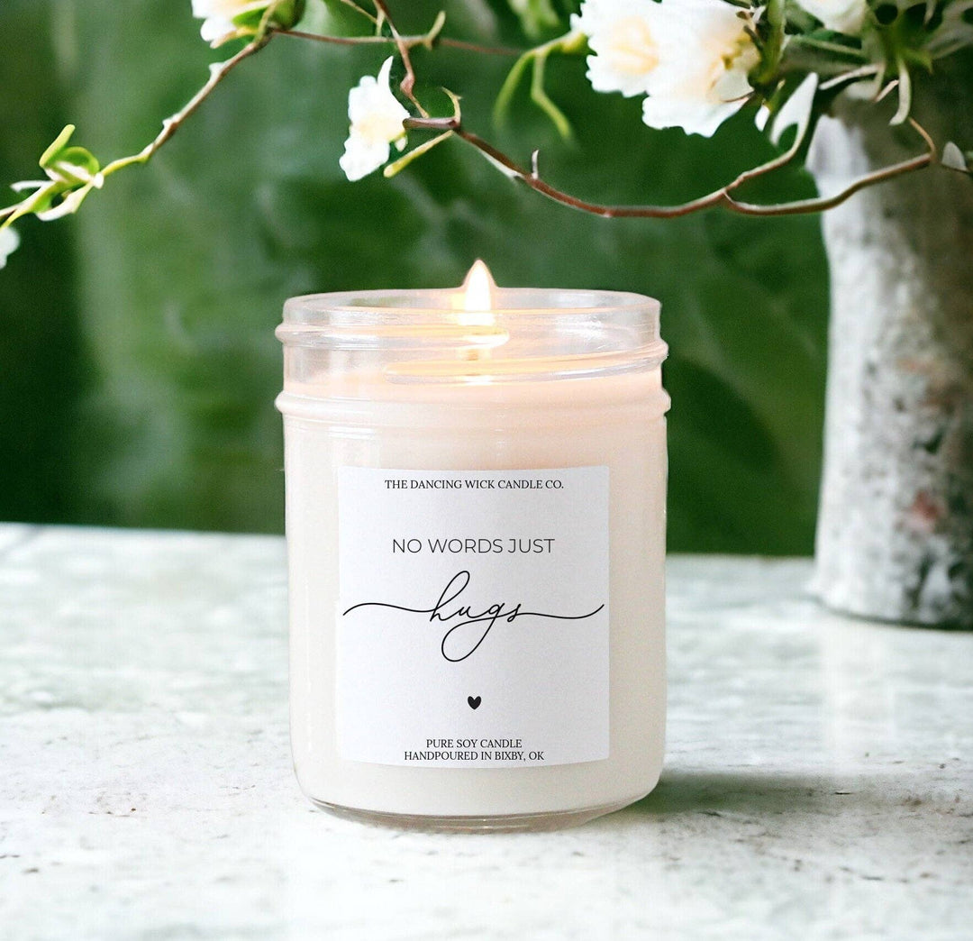 Candle in a glass jar with a label, surrounded by white flowers and greenery