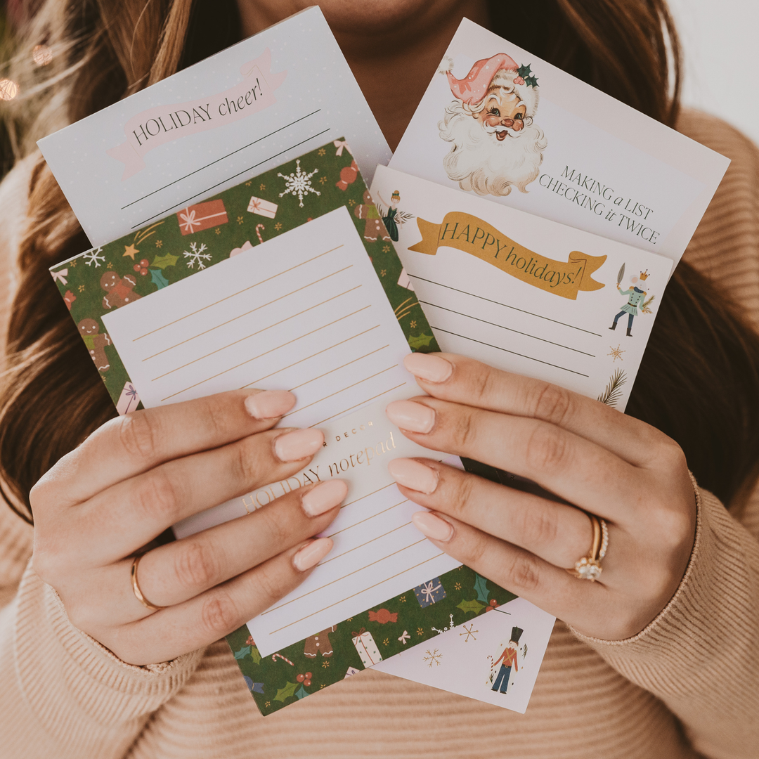 Hands holding holiday-themed notepads with decorative designs.