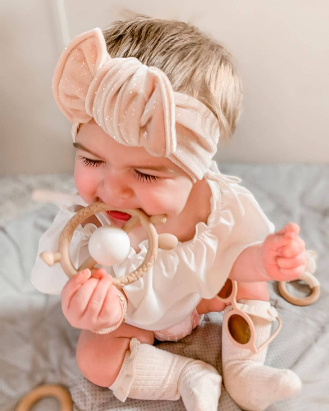 Baby wearing a pink headband and holding a teething ring on a neutral background