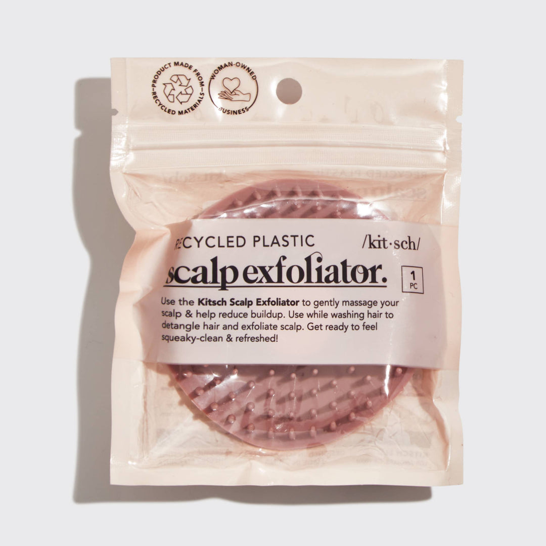 A terracotta-colored, plastic scalp exfoliator with flexible bristles in its plastic packaging with &