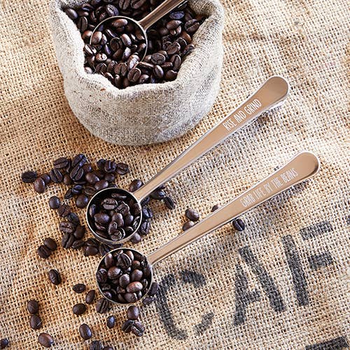 Three metal spoons filled with coffee beans on a burlap surface.