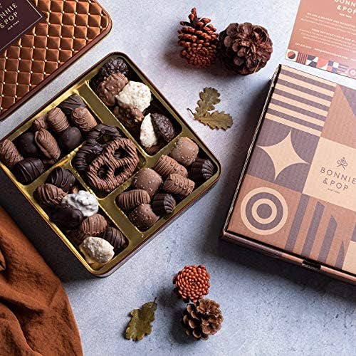 Assorted chocolates in a gold tin with decorative elements on a textured surface