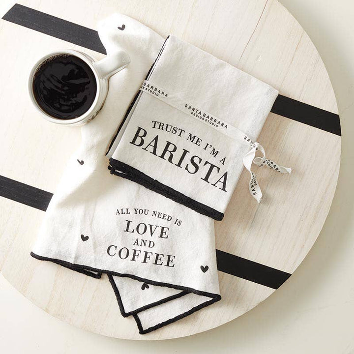 Two fabric towels with text on a wooden board with a cup of coffee.