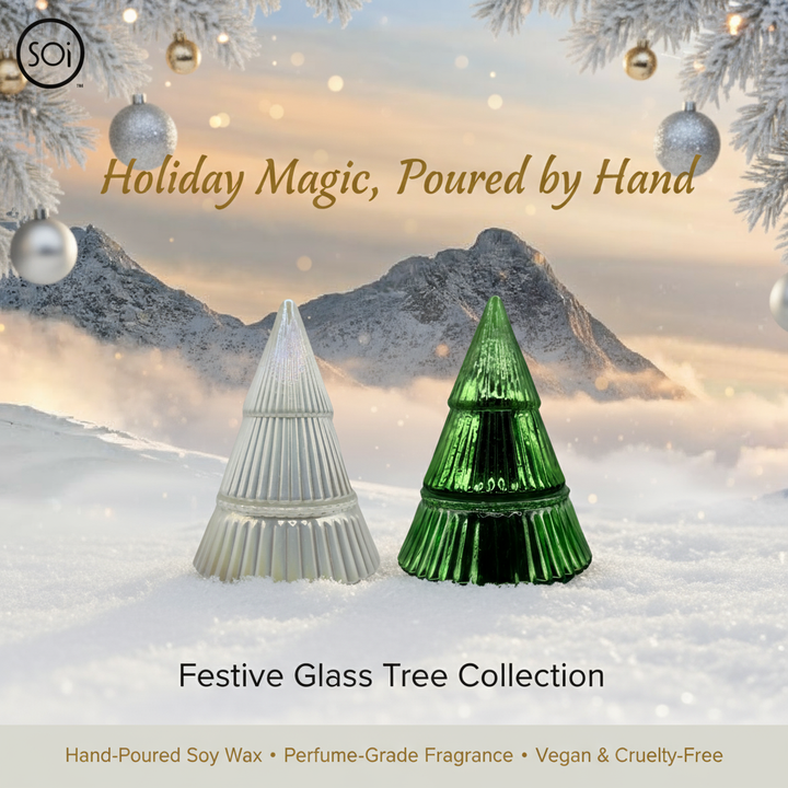 Two glass tree candles, one white and one green, in a snowy landscape with mountains and Christmas ornaments in the background.