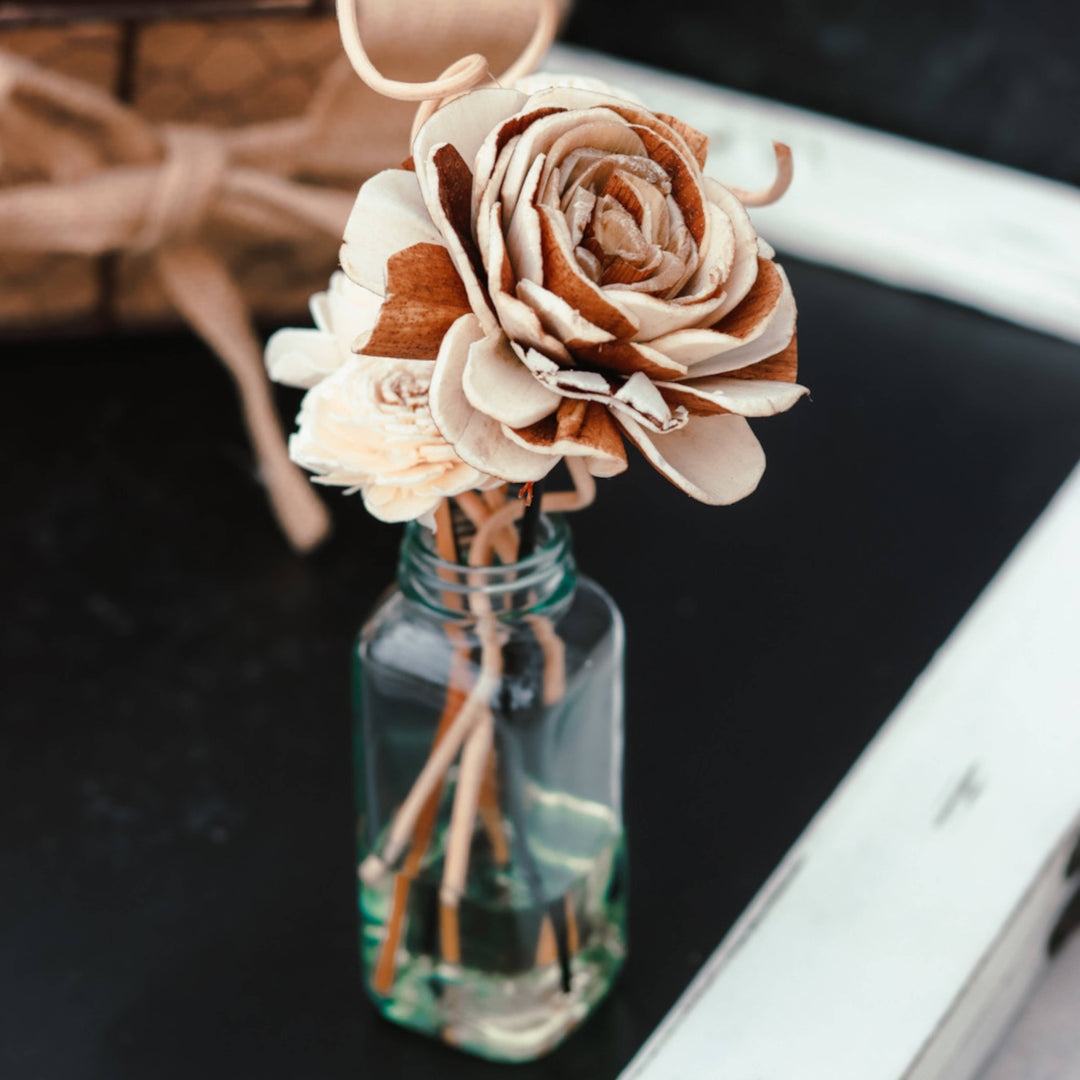 Decorative wooden flowers in a clear glass bottle on a dark surface.
