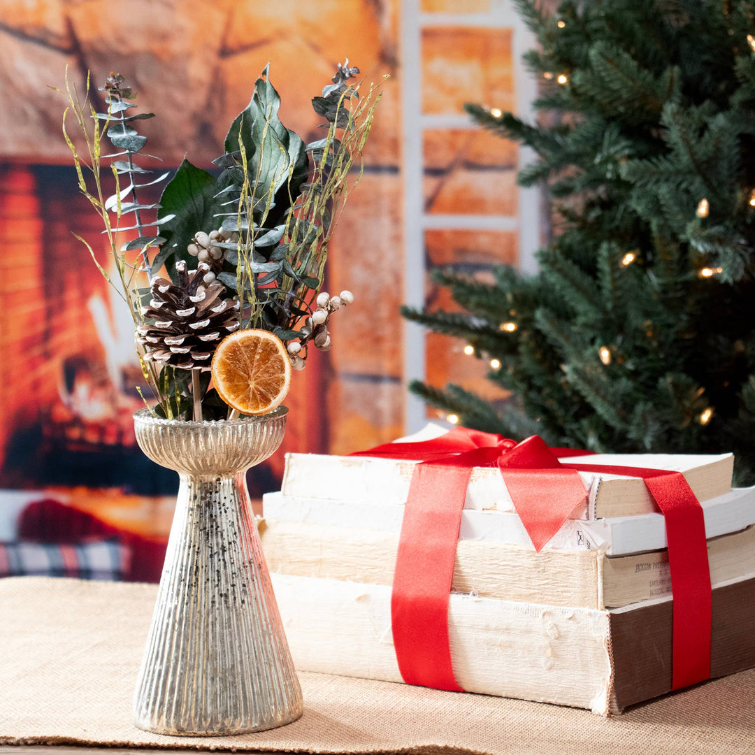 Decorative arrangement with plants and a stack of books tied with red ribbon in front of a Christmas tree.