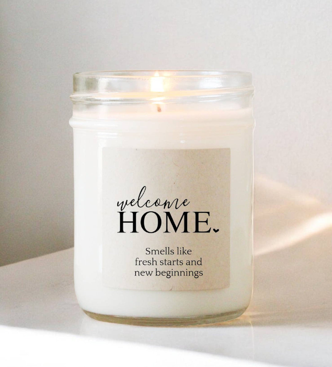 Candle in a glass jar with a 'welcome home' label on a white surface.