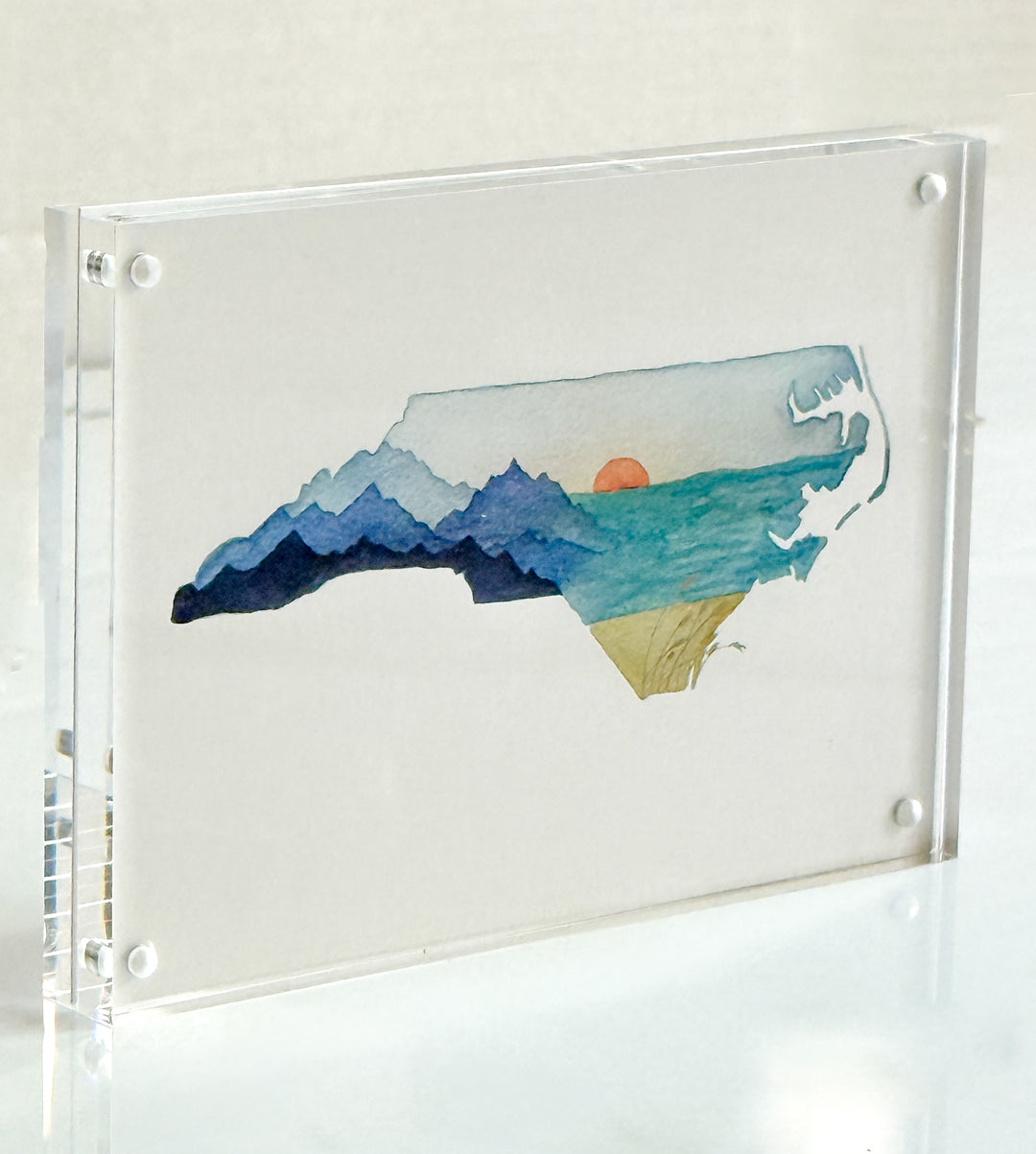 Framed artwork of a North Carolina state filled with mountain landscape with a sunset on a white background