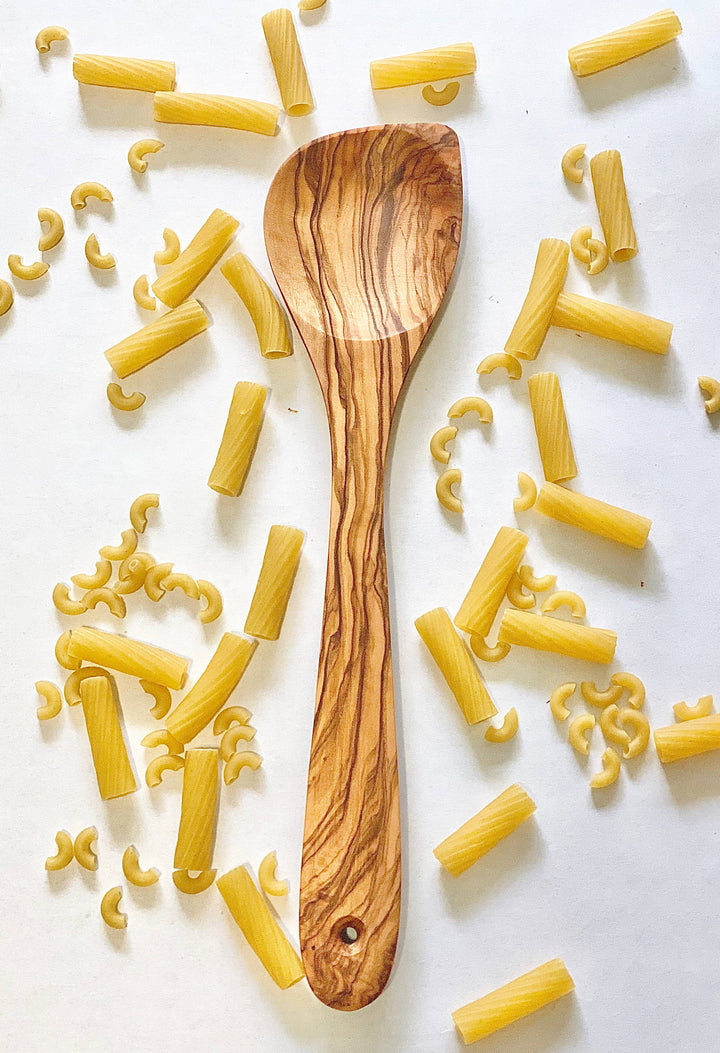 Wooden spoon surrounded by yellow pasta on a white background