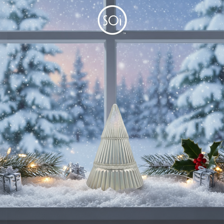 Decorative Christmas tree-shaped candle on a snowy window sill with festive decorations and SOi logo.