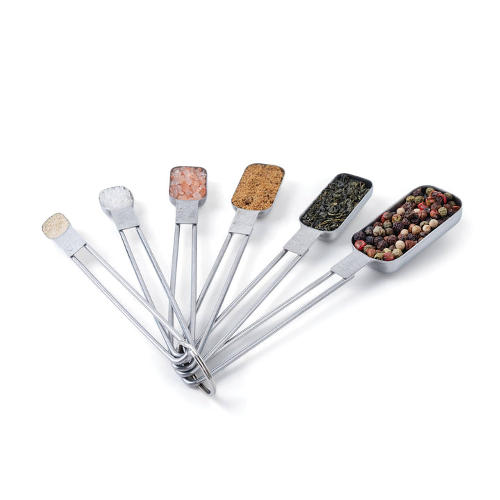 All sizes of stainless steel measuring spoons filled with different spices and herbs. 
