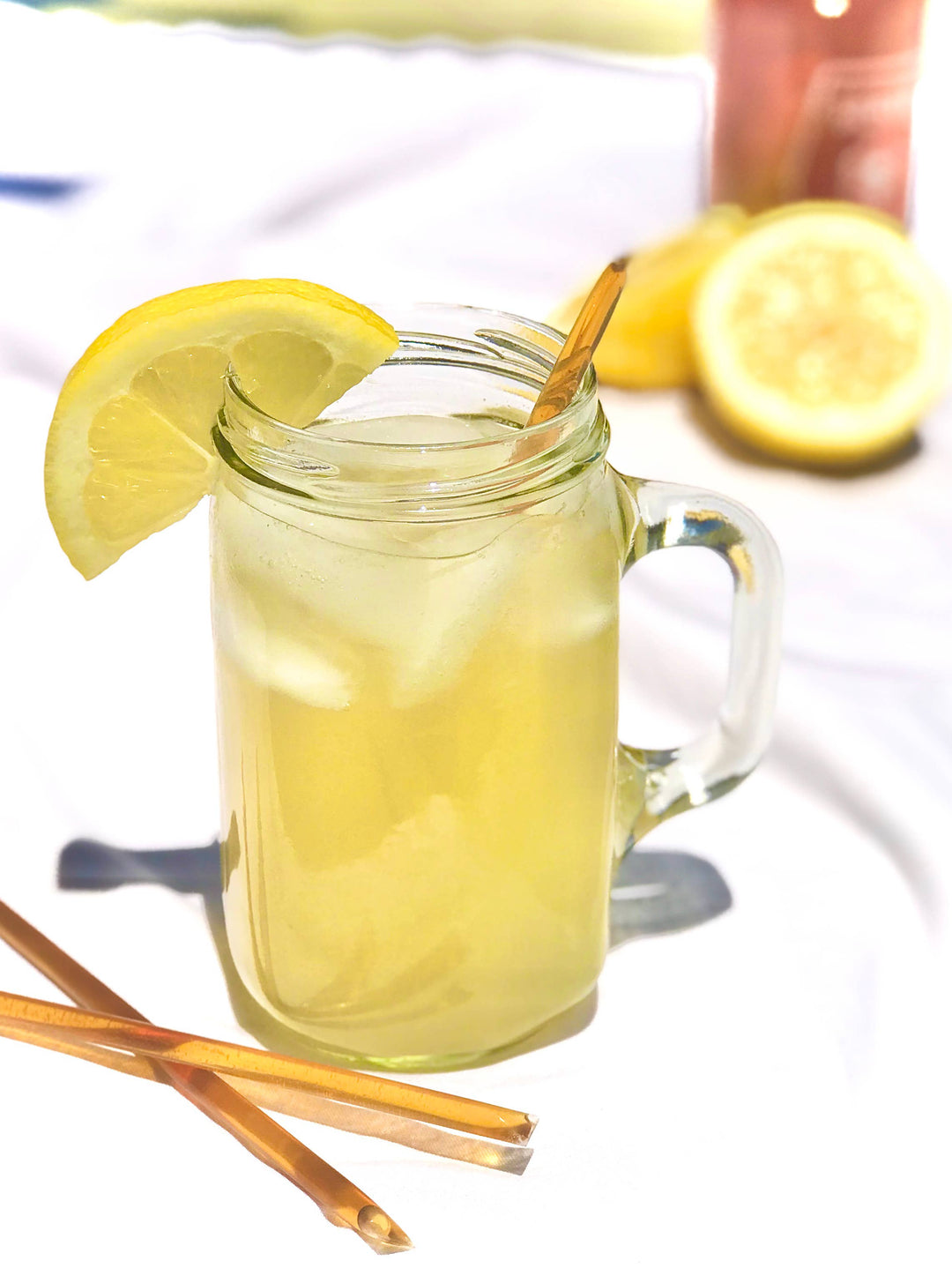 Glass mug with lemonade, lemon slice, and honey straw on a white background