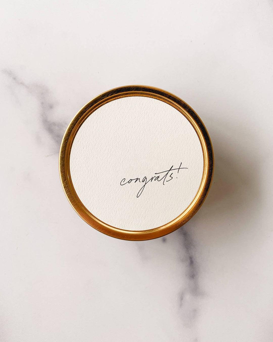 Round tin candle with 'congrats!' on a marble background