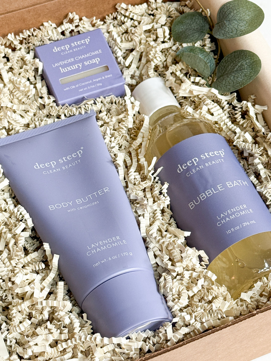 Deep Steep beauty products including body butter, soap, and bubble bath in a box with eucalyptus leaves.